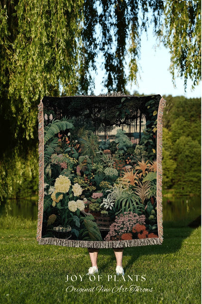 May include: A woven throw blanket featuring a detailed botanical garden scene with lush greenery, flowers, and a forest backdrop. The blanket has a fringed edge and the text "JOY OF PLANTS Original Fine Art Throws" at the bottom.