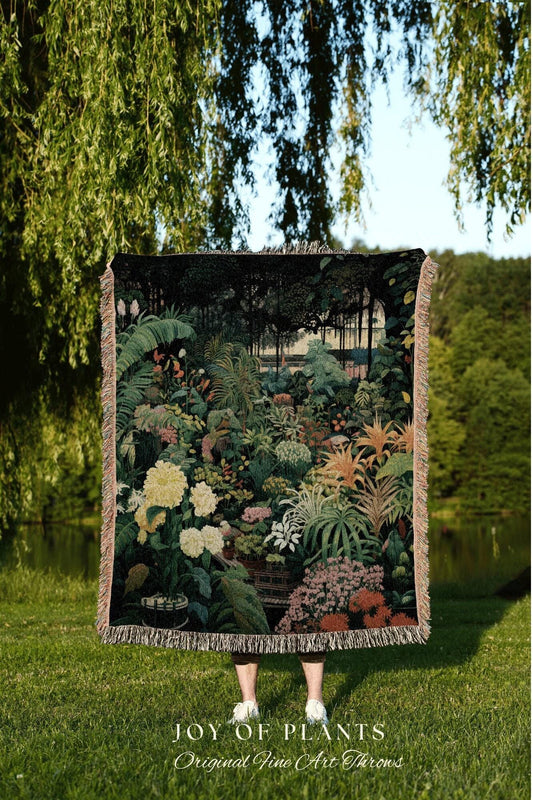 May include: A woven throw blanket featuring a detailed botanical garden scene with lush greenery, flowers, and a forest backdrop. The blanket has a fringed edge and the text "JOY OF PLANTS Original Fine Art Throws" at the bottom.