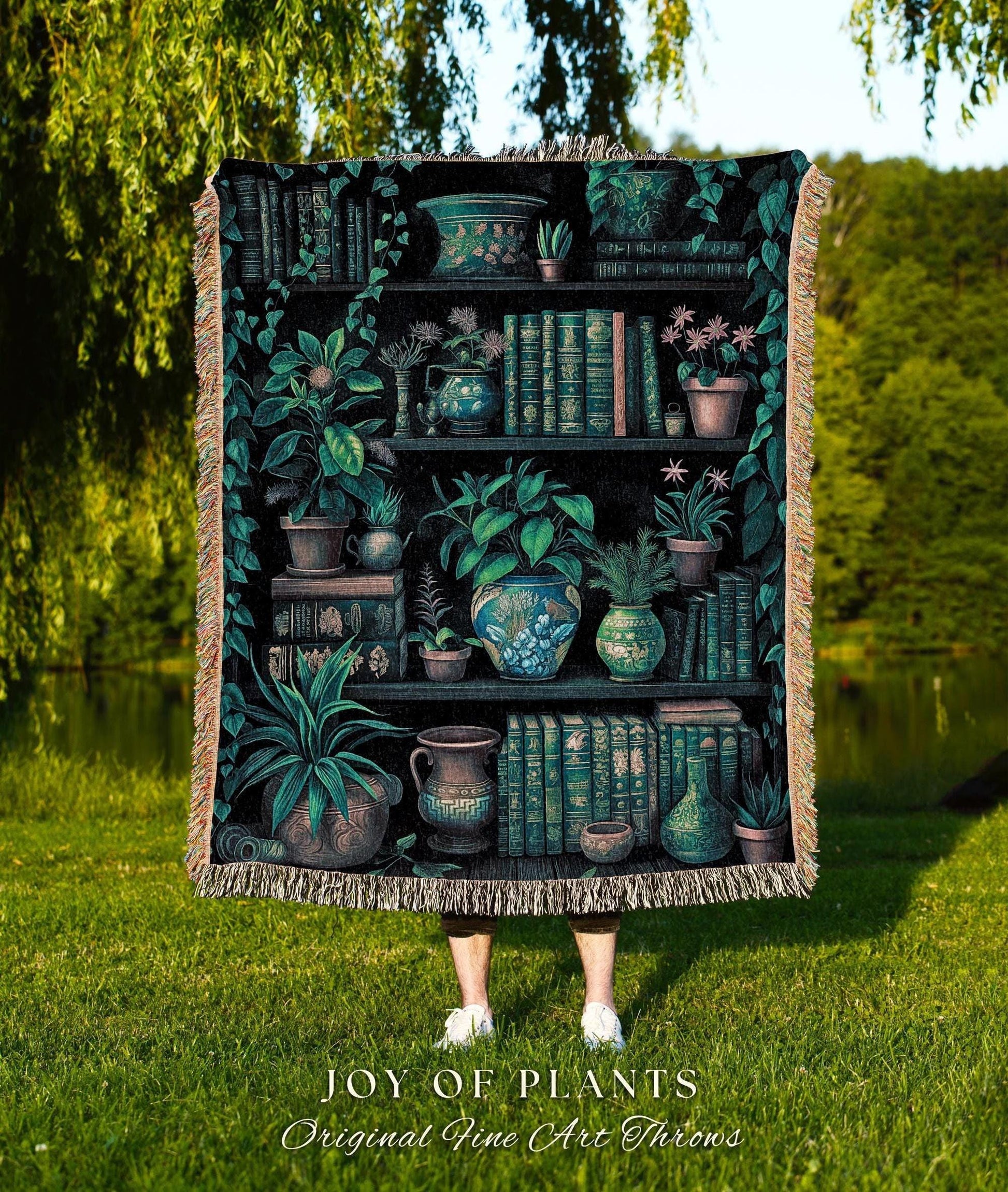 May include: A woven throw blanket featuring a detailed illustration of a bookshelf filled with plants and books. The design includes various potted plants, books, and decorative vases in shades of green and brown. The text "JOY OF PLANTS Original Fine Art Throws" is at the bottom.