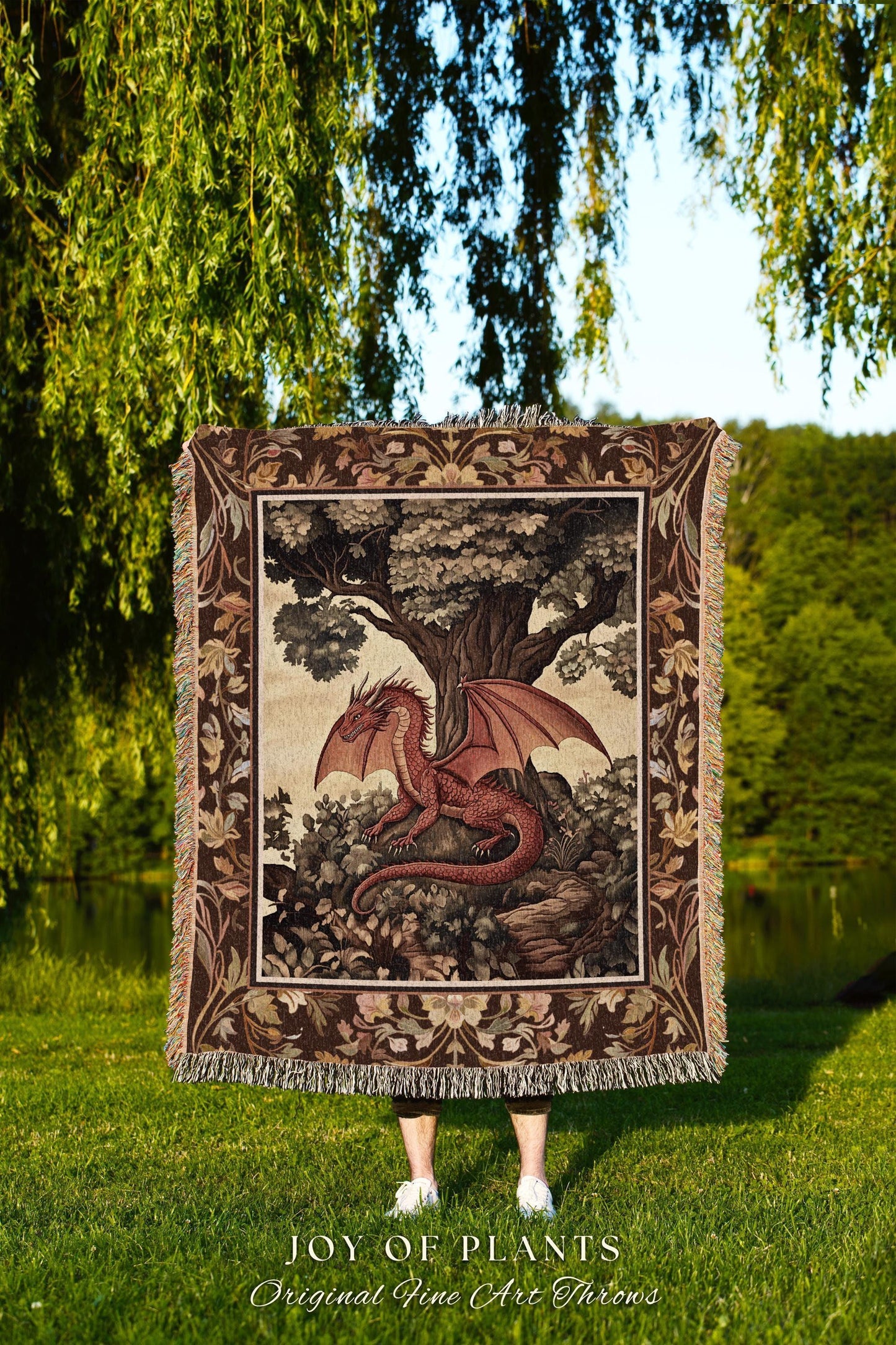 May include: A tapestry throw blanket featuring a red dragon with outstretched wings, perched beneath a large tree. The blanket has a decorative border and fringe. The text "JOY OF PLANTS Original Fine Art Throws" is at the bottom.