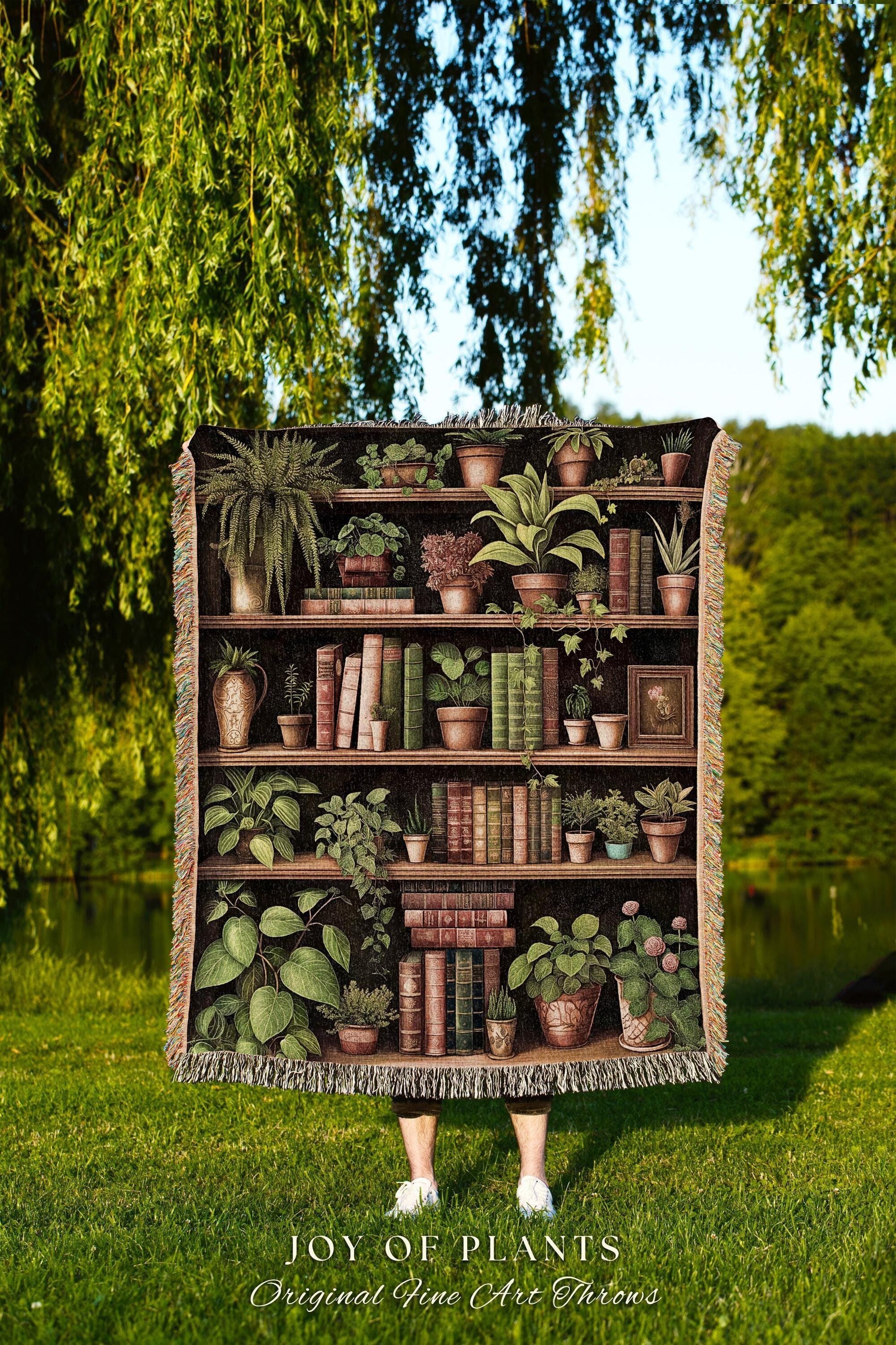 May include: A woven throw blanket featuring a detailed illustration of a bookshelf filled with potted plants and books. The blanket has a dark background and a fringed edge. The text "JOY OF PLANTS Original Fine Art Throws" is at the bottom.