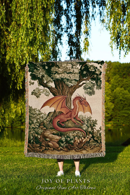 May include: A tapestry throw blanket featuring a red dragon with outstretched wings, resting in a forest setting under a large tree. The blanket has a fringed edge and the text "JOY OF PLANTS Original Fine Art Throws".