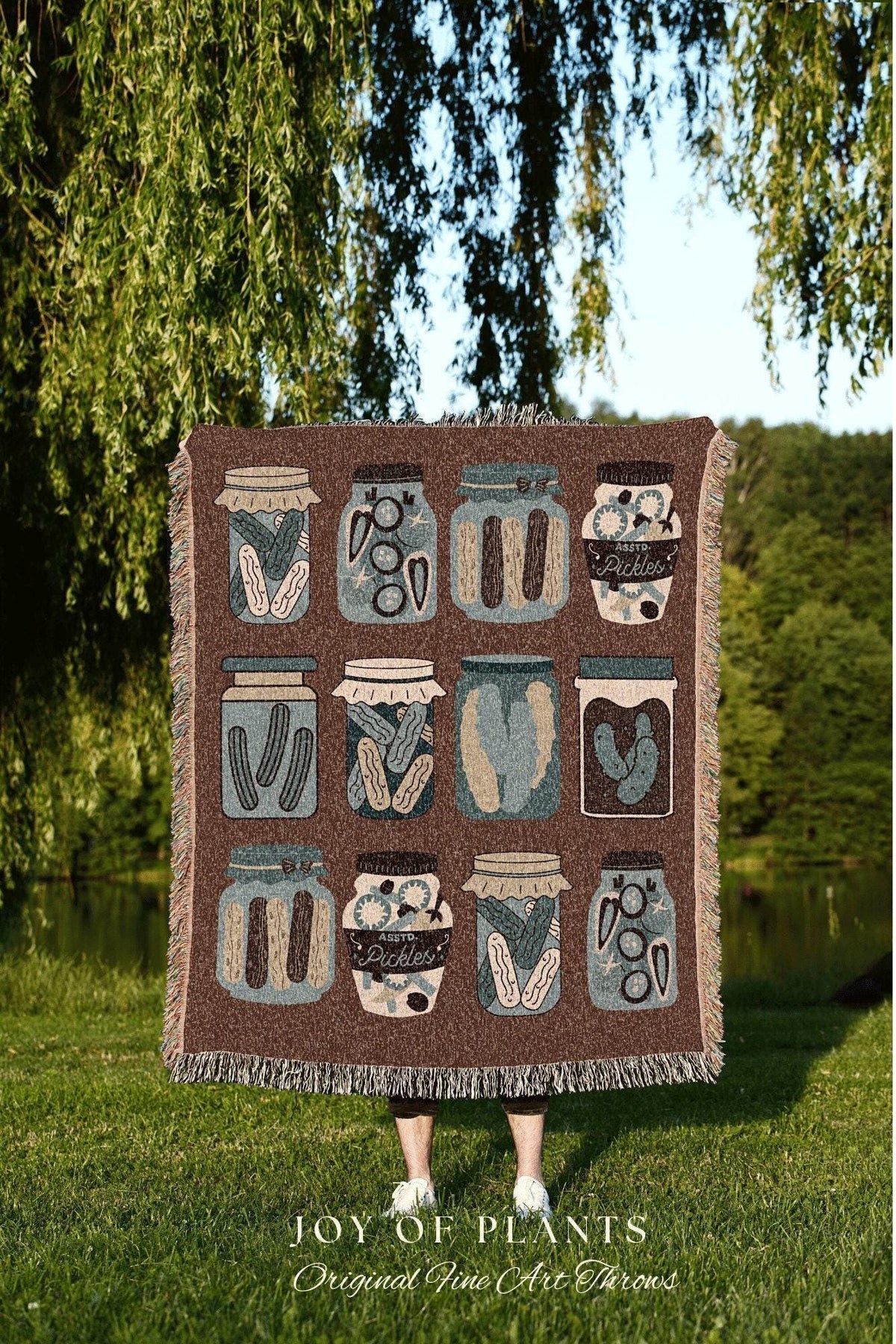 May include: A brown throw blanket featuring a repeating pattern of illustrated pickle jars in various designs and colors. The blanket has a fringed edge and the text "JOY OF PLANTS Original Fine Art Throws" at the bottom.