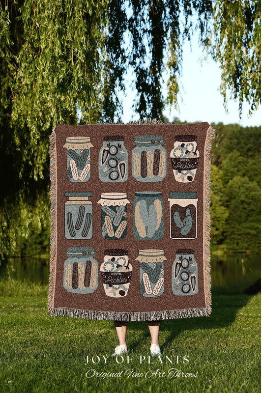 May include: A brown throw blanket featuring a repeating pattern of illustrated pickle jars in various designs and colors. The blanket has a fringed edge and the text "JOY OF PLANTS Original Fine Art Throws" at the bottom.
