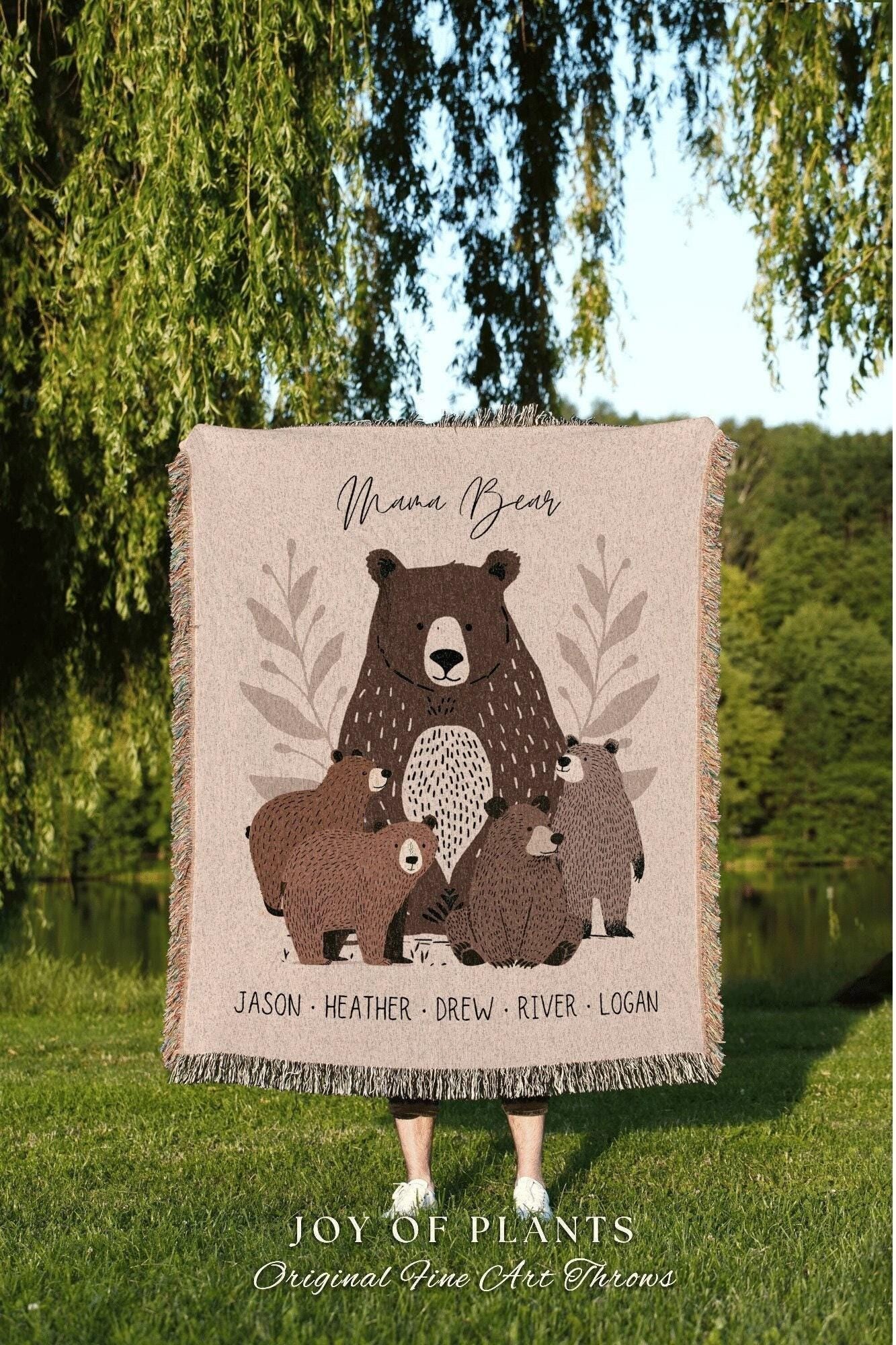 May include: Beige throw blanket featuring a Mama Bear and four bear cubs illustration. The text "Mama Bear" is above the bear family. The names Jason, Heather, Drew, River, and Logan are printed below the bears. The blanket has a fringed edge.