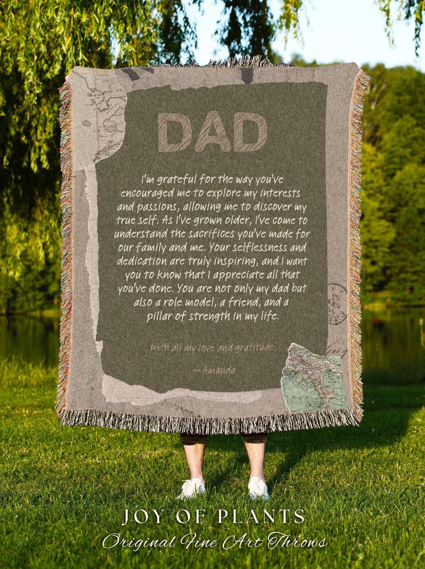 May include: A rectangular throw blanket with the word "DAD" in large, textured letters. The blanket has a message of gratitude and love, with a map design. The blanket is fringed and is held up by a person standing on green grass.