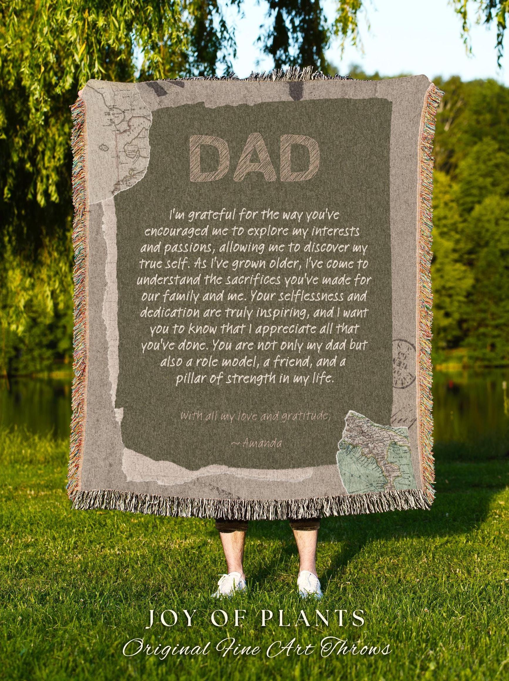 May include: A rectangular throw blanket with the word "DAD" in large, textured letters. The blanket has a message of gratitude and love, with a map design. The blanket is fringed and is held up by a person standing on green grass.
