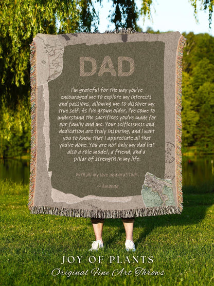May include: A rectangular throw blanket with the word "DAD" in large, textured letters. The blanket has a message of gratitude and love, with a map design. The blanket is fringed and is held up by a person standing on green grass.