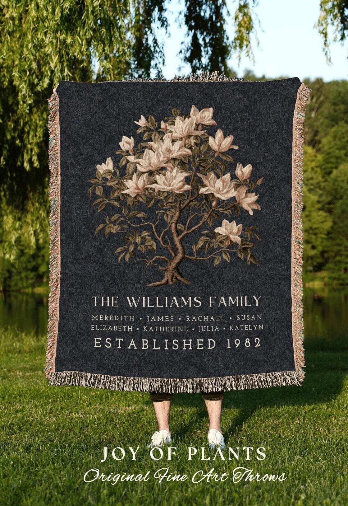May include: A dark gray throw blanket with a floral tree design and the text "THE WILLIAMS FAMILY" and "ESTABLISHED 1982". The blanket has a fringed edge and the words "JOY OF PLANTS" are at the bottom.
