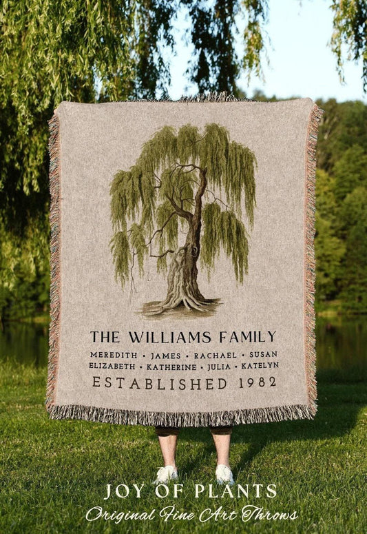 May include: A beige throw blanket featuring a detailed illustration of a weeping willow tree. The text "THE WILLIAMS FAMILY" and names are printed below the tree, with "ESTABLISHED 1982" at the bottom. The blanket has fringed edges.