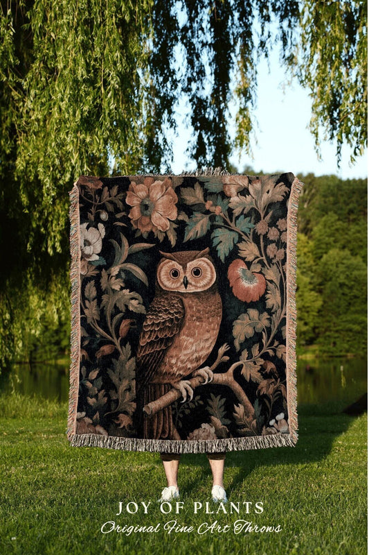 May include: A decorative throw blanket featuring a detailed illustration of a brown owl perched on a branch, surrounded by floral and foliage elements in shades of brown, green, and cream. The blanket has a dark background and a fringed edge. Text at the bottom reads "JOY OF PLANTS Original Fine Art Throws."