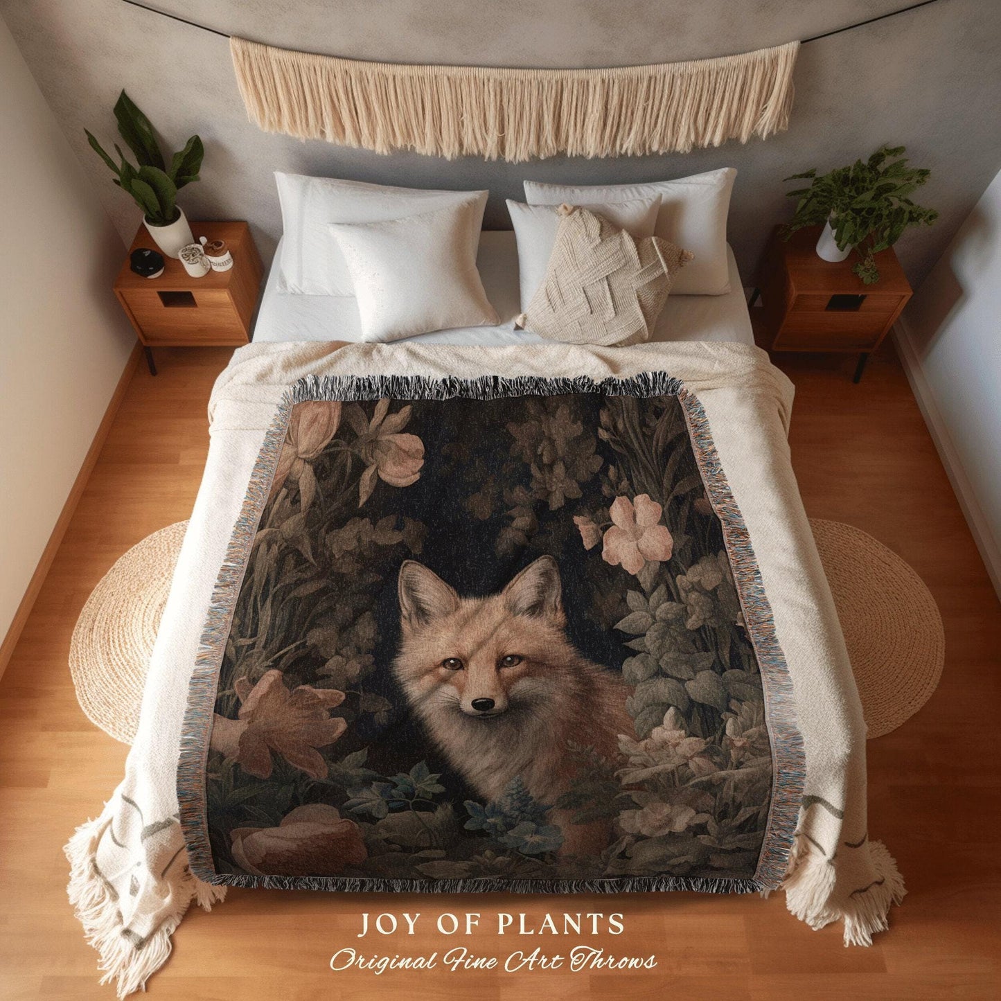 May include: A woven throw blanket featuring a fox surrounded by foliage and flowers in shades of brown, green, and cream. The blanket is draped over a bed with white bedding. The text "JOY OF PLANTS Original Fine Art Throws" is visible.