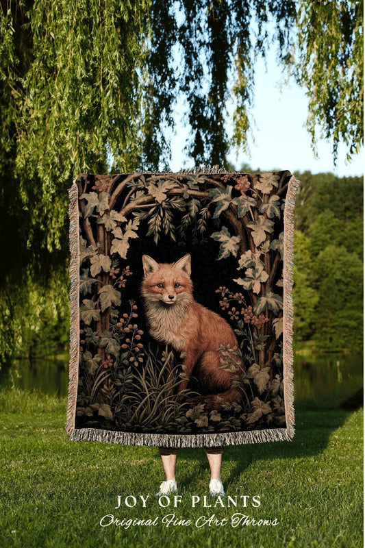 May include: A tapestry throw blanket featuring a detailed illustration of a fox in a forest setting. The throw has a black background with brown, green, and beige foliage. The text "JOY OF PLANTS Original Fine Art Throws" is at the bottom.
