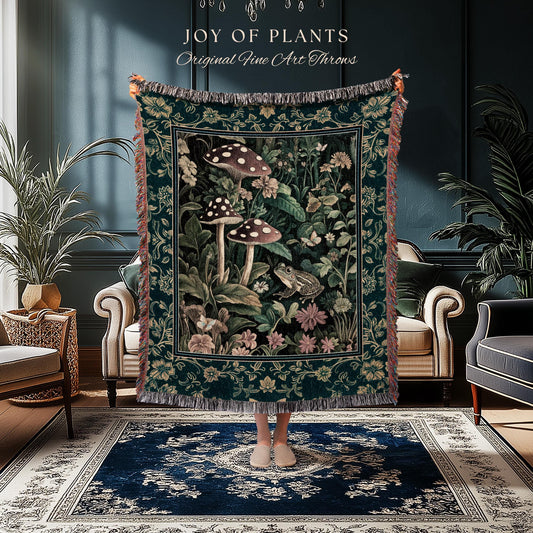 May include: A dark green throw blanket with a botanical design featuring mushrooms, flowers, and a frog. The blanket has a fringed edge and the text "JOY OF PLANTS Original Fine Art Throws" at the top.