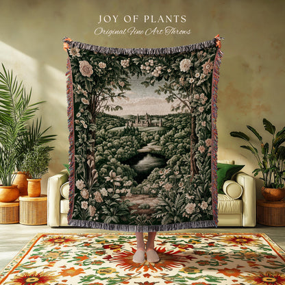 May include: A tapestry throw blanket with a landscape scene featuring a river, trees, and a castle. The throw has a dark green background with floral accents and the text "JOY OF PLANTS Original Fine Art Throws".