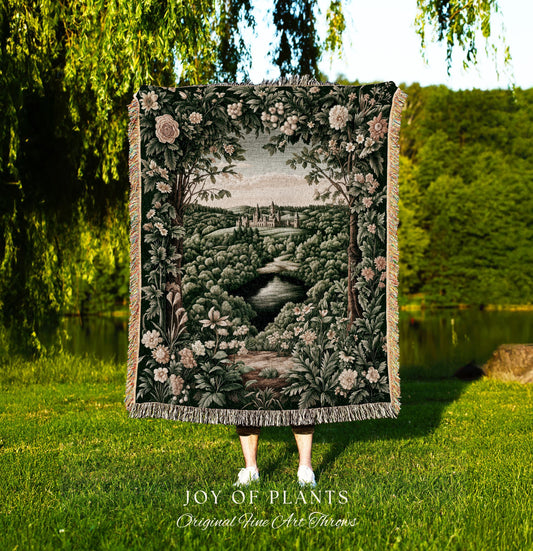 May include: A tapestry throw blanket featuring a landscape scene with a river, trees, and a castle. The blanket has a dark green background with floral and foliage details. The text "JOY OF PLANTS Original Fine Art Throws" is at the bottom.