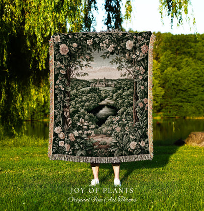 May include: A tapestry throw blanket featuring a landscape scene with a river, trees, and a castle. The blanket has a dark green background with floral and foliage details. The text "JOY OF PLANTS Original Fine Art Throws" is at the bottom.
