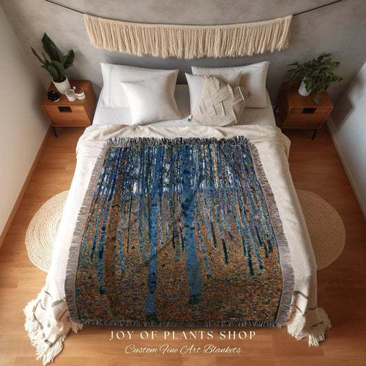 May include: A woven blanket featuring a forest scene with tall, slender trees in shades of blue and brown. The blanket has a fringed edge and is displayed on a bed with white bedding. The text "JOY OF PLANTS SHOP Custom Fine Art Blankets" is at the bottom.