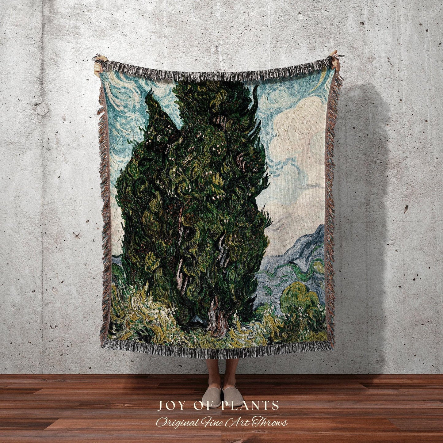 May include: A woven throw blanket featuring a landscape painting of a tall green tree under a blue sky with white clouds. The blanket has a fringed edge and the text "JOY OF PLANTS Original Fine Art Throws".