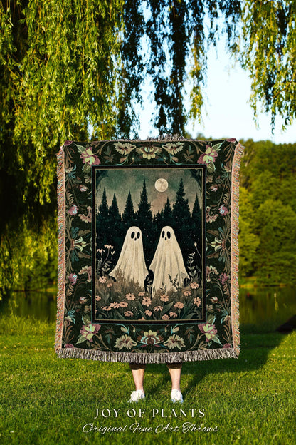May include: A decorative throw blanket featuring a forest scene with two ghost figures under a full moon. The blanket has a dark green floral border and fringe. The text "JOY OF PLANTS Original Fine Art Throws" is at the bottom.