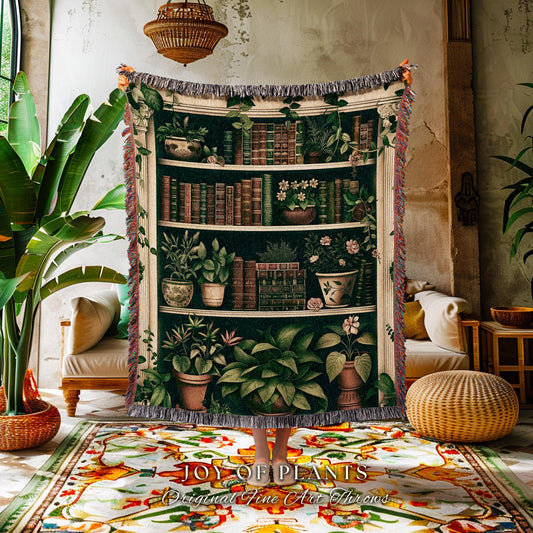 May include: A woven throw blanket featuring a detailed illustration of a bookshelf filled with plants and books. The design includes various potted plants and stacks of books in shades of green, brown, and white. The blanket has a fringed edge.