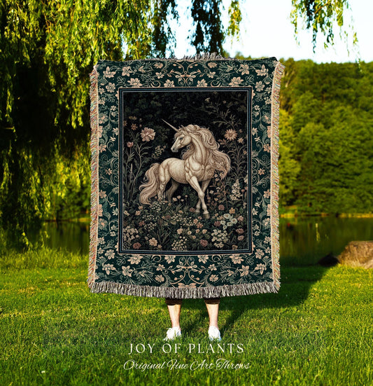 May include: A tapestry throw blanket featuring a white unicorn in a floral garden. The blanket has a dark green border with floral patterns and fringe. The text "JOY OF PLANTS Original Fine Art Throws" is at the bottom.