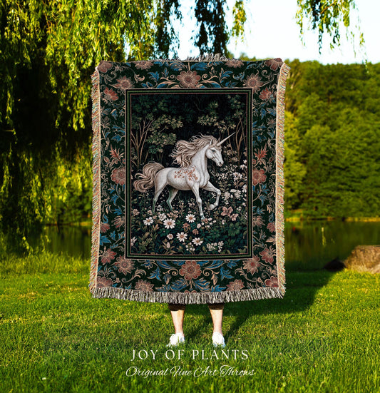 May include: A tapestry throw blanket featuring a white unicorn in a forest scene with flowers. The blanket has a dark green background with floral borders and fringe. The text "JOY OF PLANTS Original Fine Art Throws" is at the bottom.
