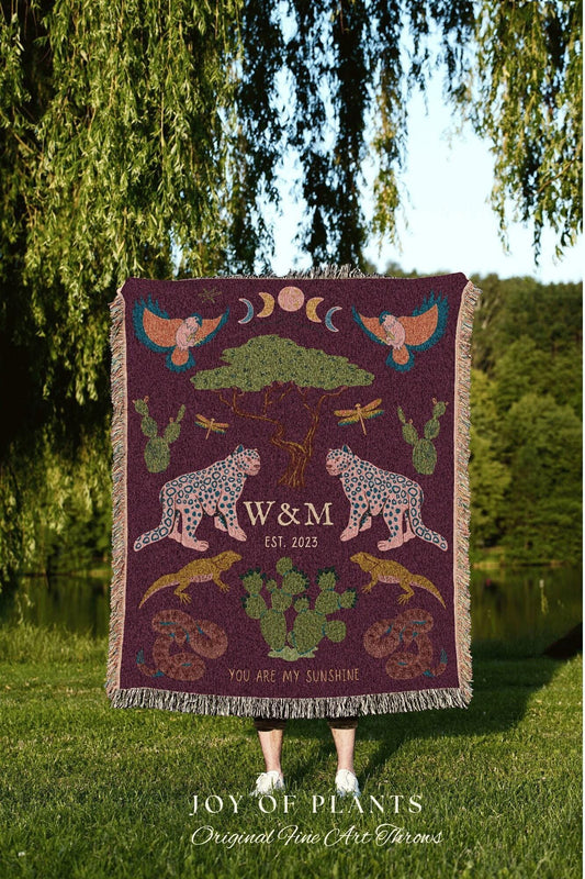 May include: A burgundy throw blanket with a nature-themed design. It features illustrations of leopards, cacti, birds, and the text "W&M EST. 2023" and "YOU ARE MY SUNSHINE". The blanket has a fringed edge and the text "JOY OF PLANTS Original Fine Art Throws".