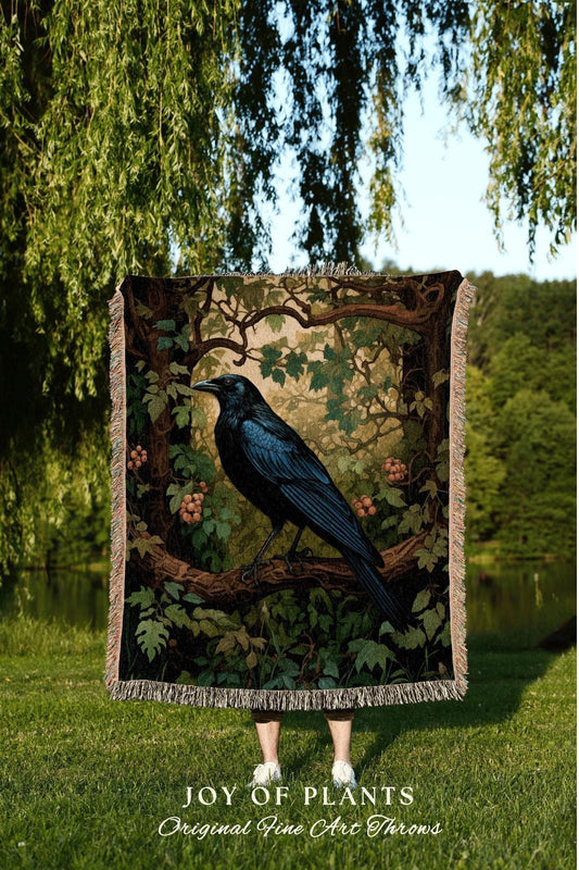 May include: A tapestry throw blanket featuring a detailed illustration of a black raven perched on a branch, surrounded by foliage and berries. The blanket has a fringed edge and the text "JOY OF PLANTS Original Fine Art Throws" at the bottom.
