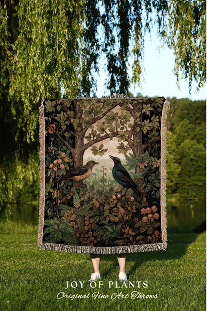 May include: A woven throw blanket featuring a detailed illustration of two birds perched in a forest scene with trees, foliage, and flowers. The color palette includes shades of brown, green, and beige. The text "JOY OF PLANTS Original Fine Art Throws" is at the bottom.