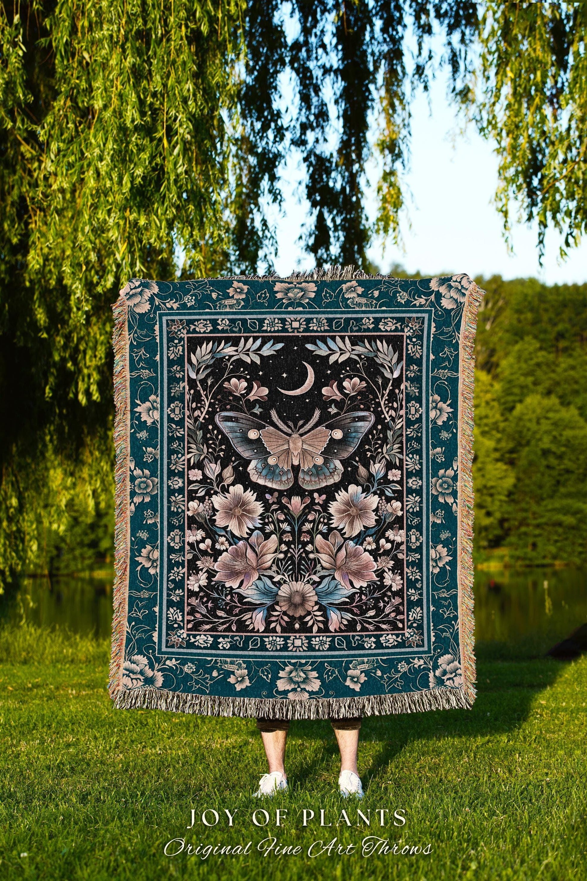 May include: A teal and black throw blanket with a floral and moth design. The blanket features a central moth image with a crescent moon and floral accents. The text "JOY OF PLANTS Original Fine Art Throws" is at the bottom.