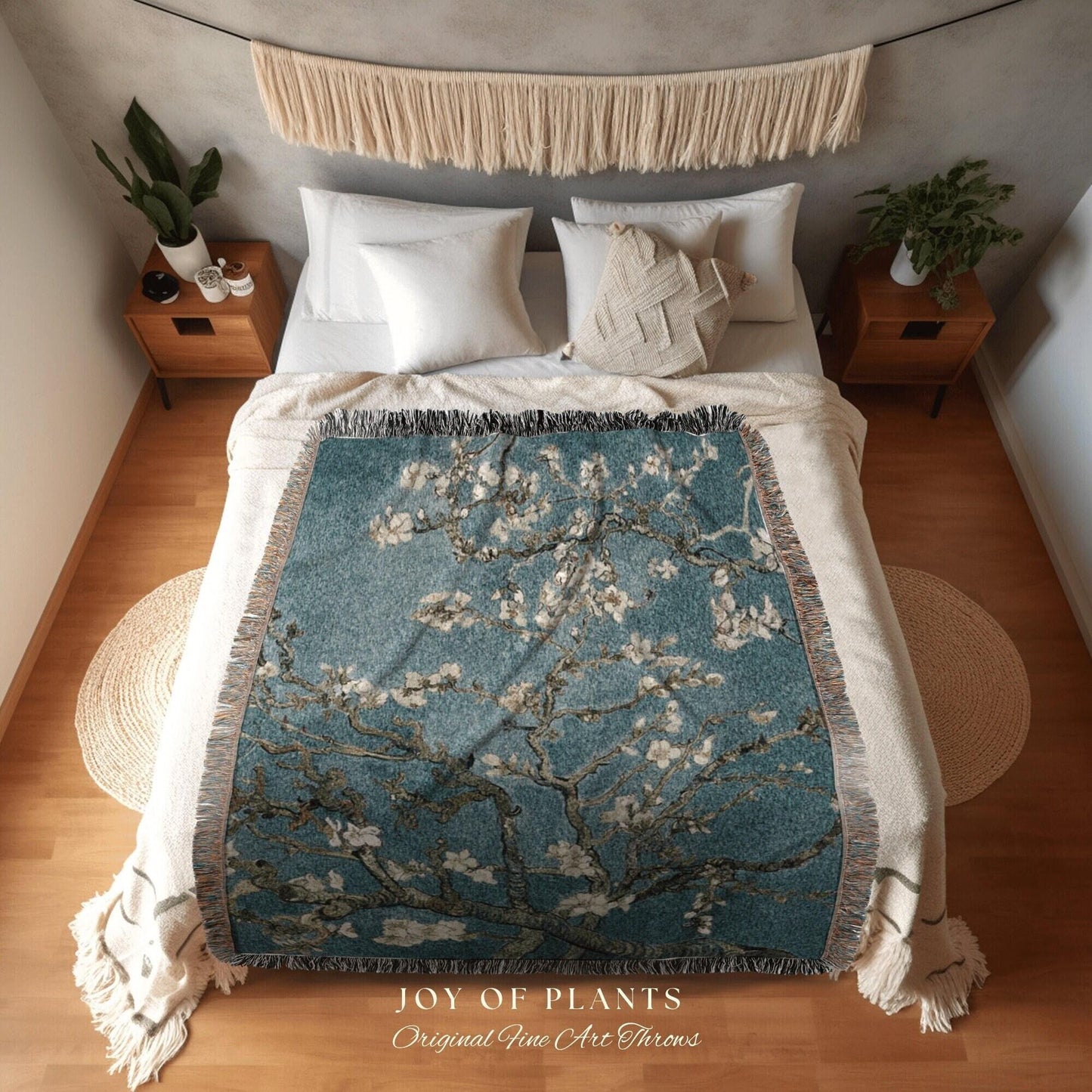 May include: A teal throw blanket with a floral design, draped over a bed. The blanket features a tree with white blossoms against a teal background. The text "JOY OF PLANTS Original Fine Art Throws" is visible.
