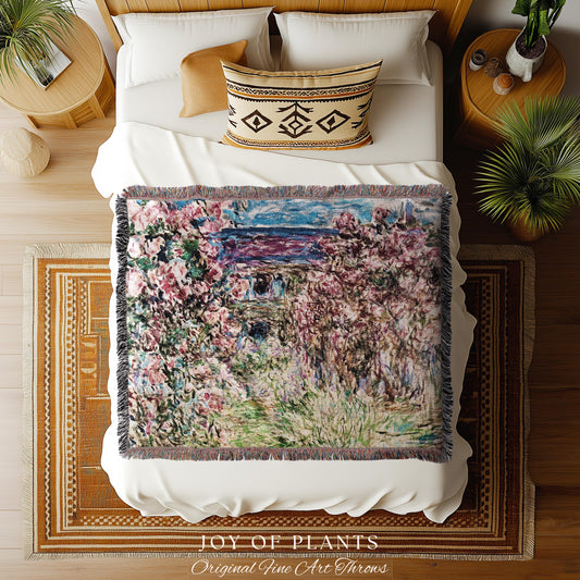 May include: A woven throw blanket with a floral painting design in shades of pink, green, and blue. The blanket has a fringed edge and is displayed on a white bed. The text "JOY OF PLANTS Original Fine Art Throws" is at the bottom.
