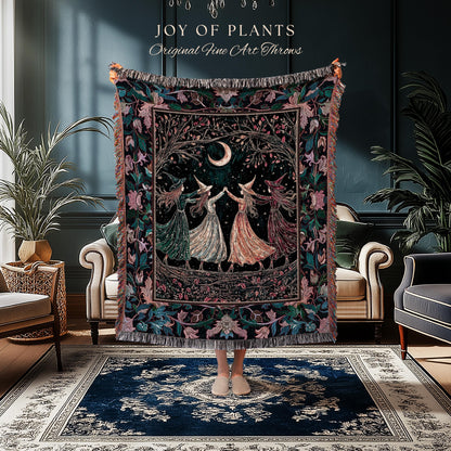 May include: A decorative throw blanket featuring a dark color palette with a central image of witches dancing under a crescent moon. The blanket has a fringed edge and the text "JOY OF PLANTS Original Fine Art Throws".