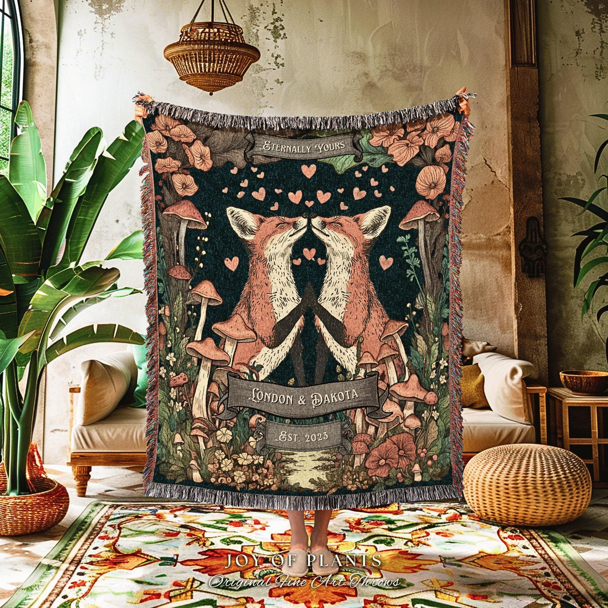 May include: A woven throw blanket featuring a forest scene with two kissing foxes, mushrooms, and floral elements. The blanket has a dark background with the text "Eternally Yours", "London & Dakota", and "Est. 2023". The blanket has a fringed edge.