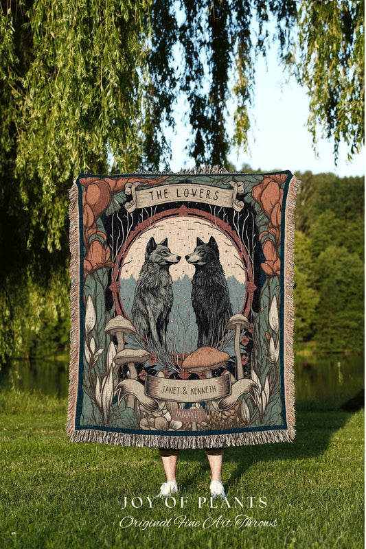 May include: A woven throw blanket featuring a design with two wolves facing each other, framed by mushrooms and foliage. The words "THE LOVERS" are at the top, with "JANET & KENNETH" and "MMXXIII" below. The blanket has a fringed edge.