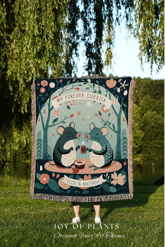 May include: A woven throw blanket with a whimsical illustration of two mice holding a candle, with the text "MY FOREVER SIDEKICK" and "ELISE & MATTHEW". The blanket has a teal background with floral and tree motifs. The bottom of the blanket has a fringe.