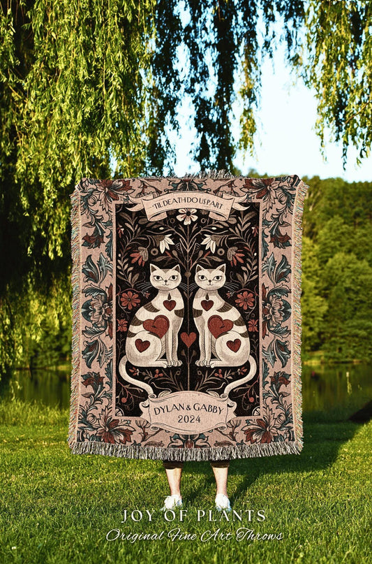 May include: A decorative throw blanket featuring two white cats with heart-shaped markings, set against a dark floral background. The blanket includes the text "'TIL DEATH DO US PART" and "DYLAN & GABBY 2024". The bottom of the blanket reads "JOY OF PLANTS Original Fine Art Throws".