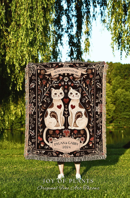 May include: A decorative throw blanket featuring two white cats with heart-shaped accents, framed by floral and scroll designs. The blanket has the text "'TIL DEATH DO US PART" and "DYLAN & GABBY 2024". The blanket has a fringed edge.