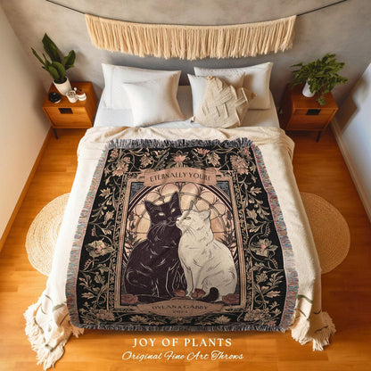 May include: A black and cream throw blanket featuring a design of two cats, one black and one white, with the text "Eternally Yours" and "Dylan & Gabby 2023". The blanket has a floral border and the words "Joy of Plants Original Fine Art Throws".