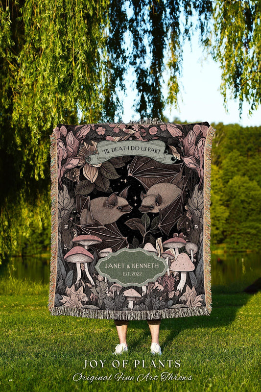 May include: A woven throw blanket with a dark background featuring bats, mushrooms, and floral elements. The blanket includes the text "TIL DEATH DO US PART" and the names "JANET & KENNETH EST. 2022". The bottom of the blanket reads "JOY OF PLANTS Original Fine Art Throws".