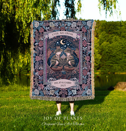 May include: A tapestry throw blanket with a detailed illustration of two frogs wearing crowns, beneath a crescent moon. The blanket features the text "UNTIL WE CROAK" and "DYLAN & GABBY 2025". The blanket has a floral border and fringe.