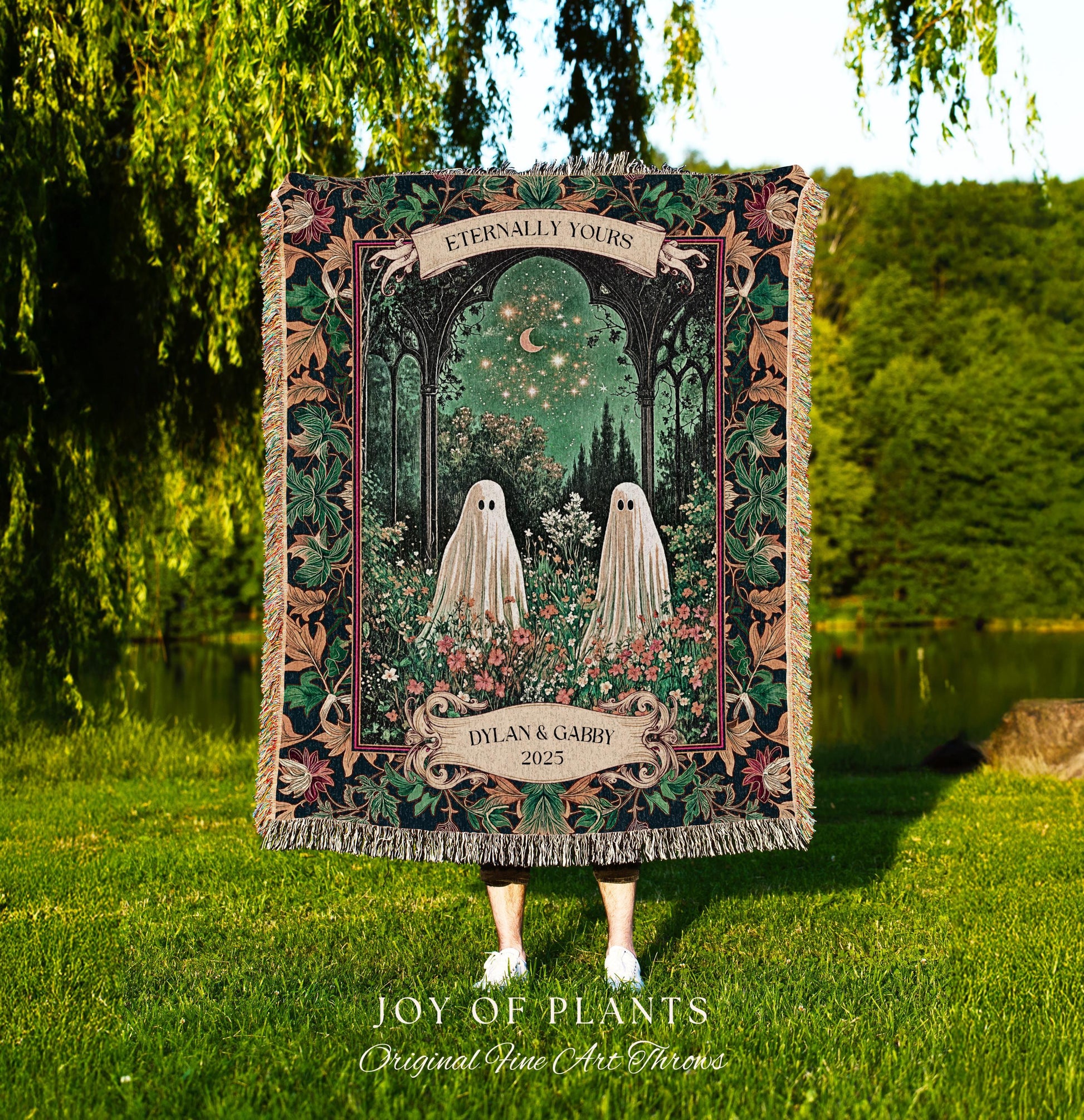 May include: A decorative throw blanket featuring a whimsical design with two ghost figures in a garden setting. The blanket has a dark border with floral and leaf patterns, and the text "Eternally Yours" and "Dylan & Gabby 2025". The blanket is fringed.