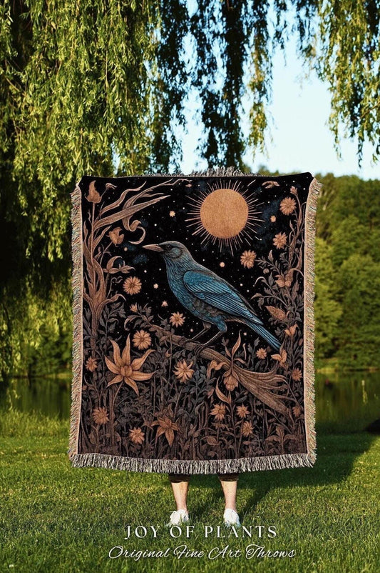 May include: A black throw blanket with a celestial design featuring a blue bird perched on a branch, a golden sun, and floral elements. The blanket has a fringed edge and the text "JOY OF PLANTS Original Fine Art Throws".