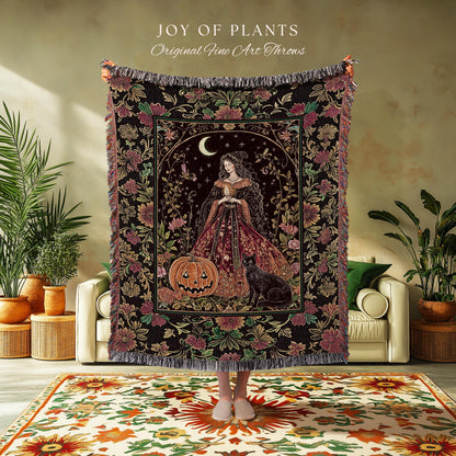May include: A decorative throw blanket with a dark background and a central image of a woman in a gown, a jack-o'-lantern, and a black cat. The blanket has a floral border and the text "JOY OF PLANTS Original Fine Art Throws".