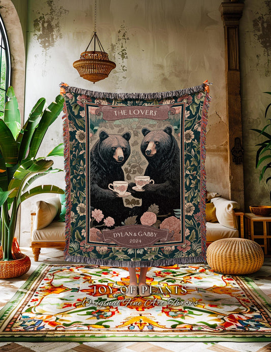 May include: A woven tapestry throw blanket featuring two bears holding teacups, with the text "THE LOVERS" and "DYLAN & GABBY 2024". The blanket has a dark green background with floral and leaf patterns, and a fringed edge.