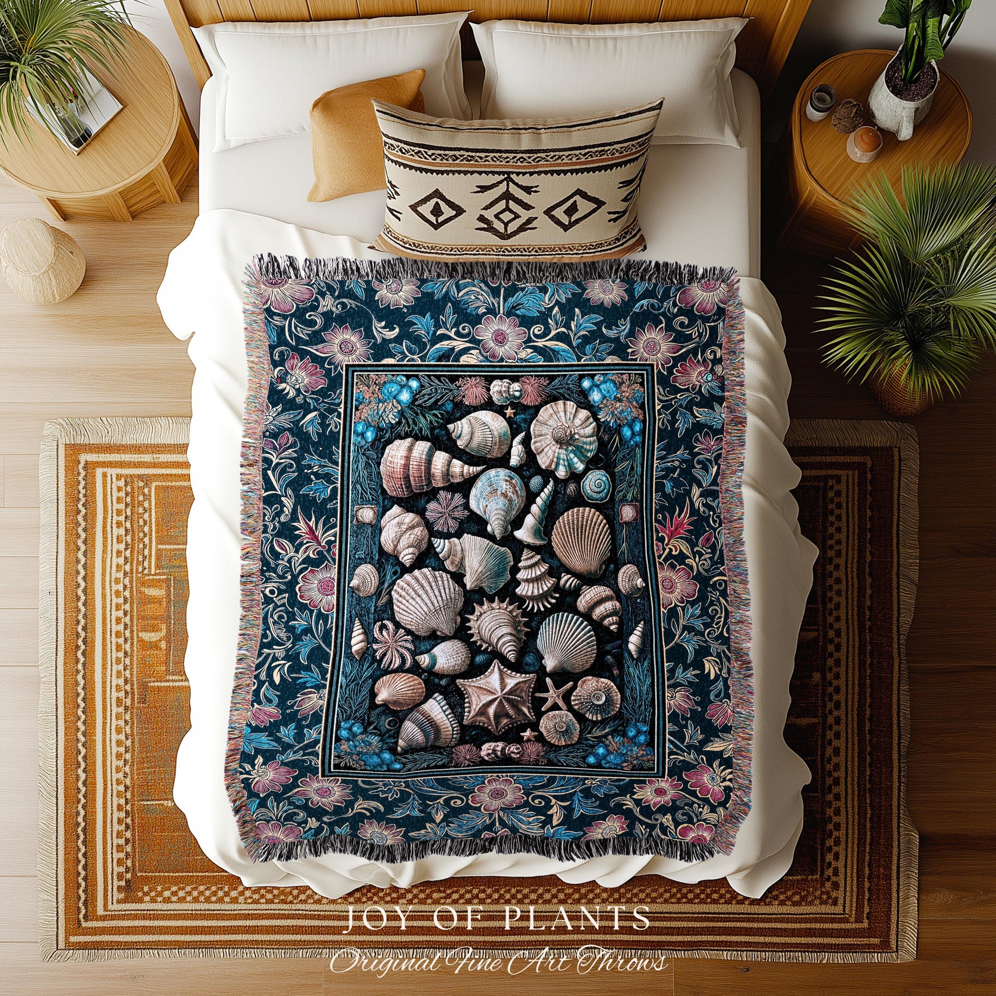 May include: A dark blue throw blanket with a seashell design and floral border. The blanket features various seashells in shades of white, tan, and gray. The text "JOY OF PLANTS Original Fine Art Throws" is at the bottom.