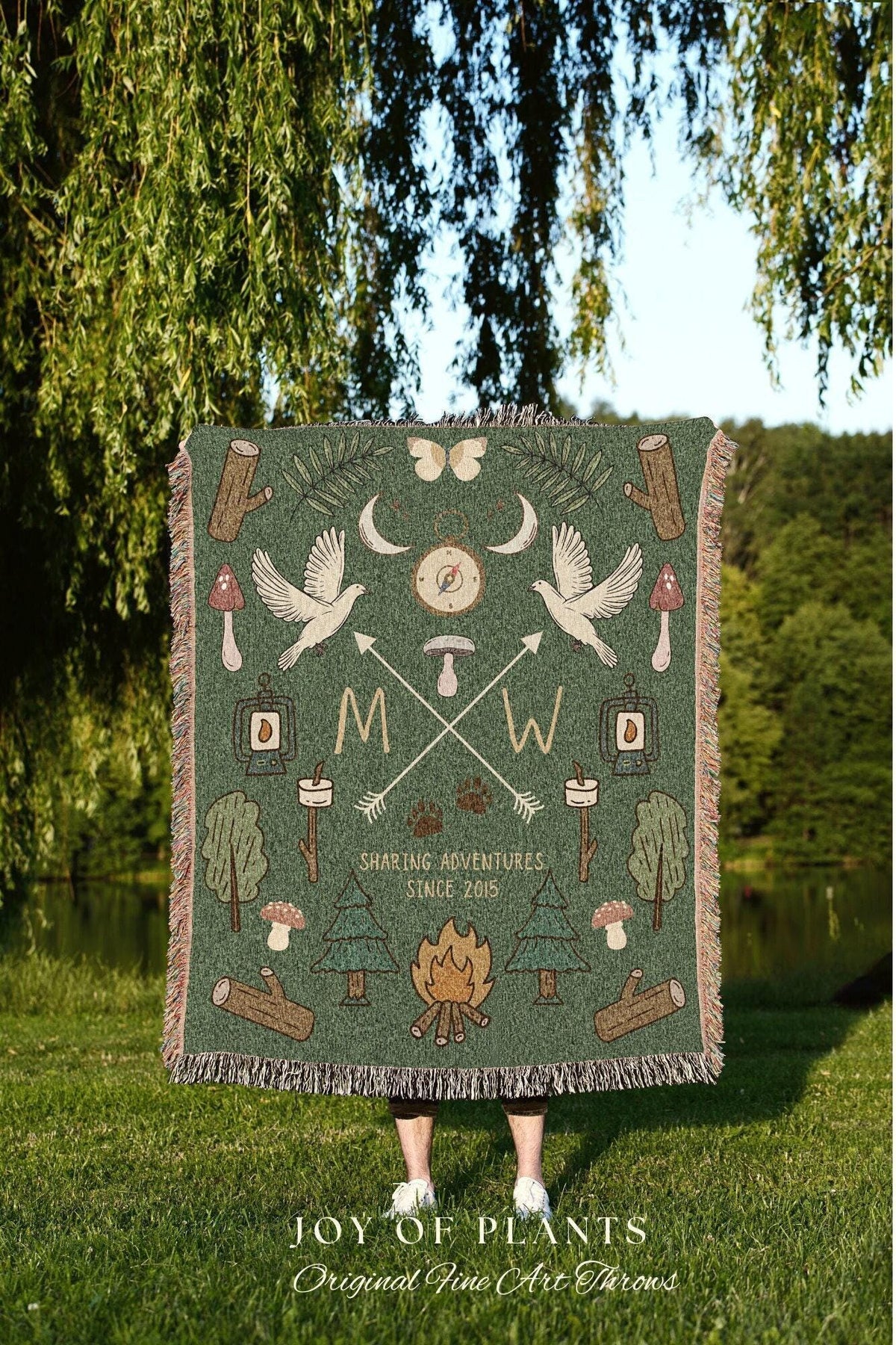 May include: Green throw blanket with a nature-themed design. Features illustrations of birds, arrows, trees, and a campfire. Text includes "Sharing Adventures Since 2015" and "Joy of Plants".