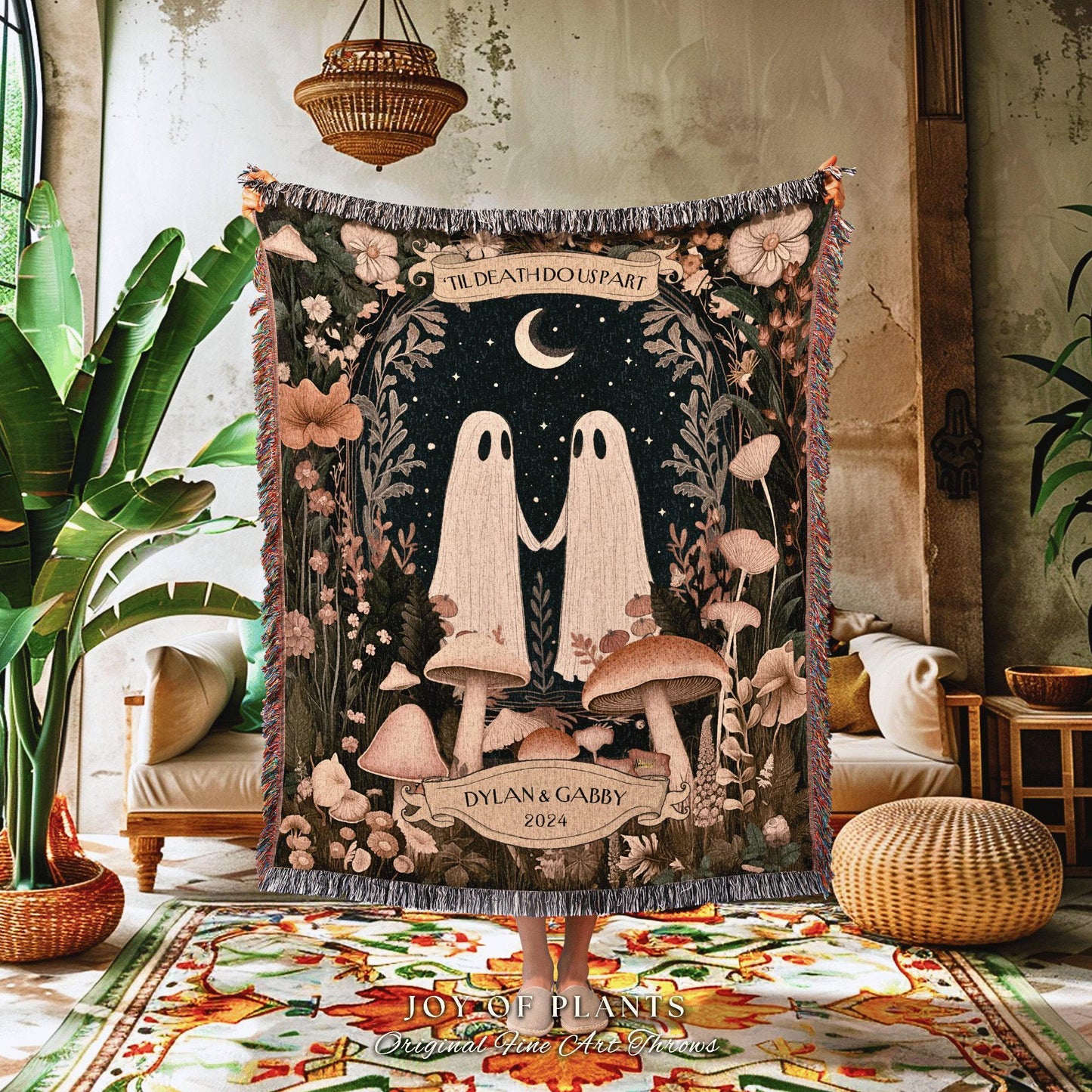 May include: A decorative tapestry featuring a whimsical design with two ghost figures holding hands under a crescent moon. The tapestry includes the text "TIL DEATH DO US PART" and the names "DYLAN & GABBY 2024". The color palette includes shades of green, brown, and cream.