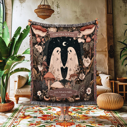 May include: A woven throw blanket featuring a whimsical design with two ghost figures holding hands under a crescent moon and stars. The blanket has a dark background with floral and mushroom accents, and the text "FOREVER & ALWAYS" and "DYLAN & GABBY 2024".